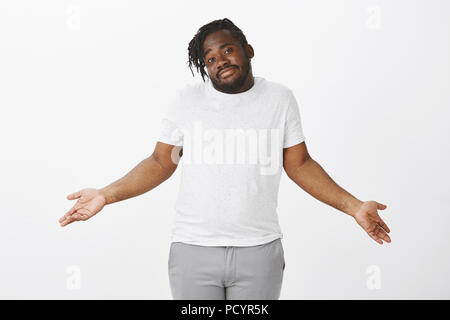 Nessuna idea di ciò che sta accadendo. Ritratto di spensierata affascinante ragazzo grassoccio in abito casual, scrollare con diffusione palme e testa inclinata, essendo inconsapevoli e cl Foto Stock