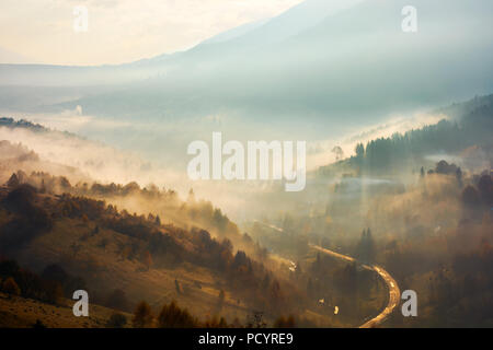 Bellissimo sfondo velato. paese strada giù nella valle di alberi sulla collina nella nebbia Foto Stock