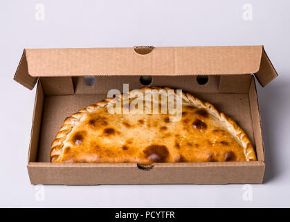 Chiuso calzone di pizza nella scatola di imballaggio su sfondo grigio. Foto Stock