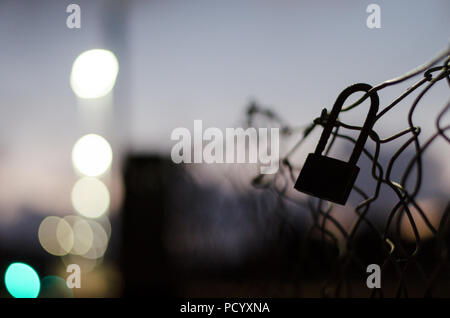 Close up di un lucchetto bloccato per una catena recinzione al blue ora con luce morbida in background Foto Stock