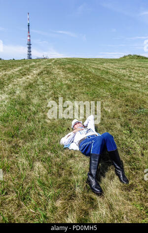 Uomo in costumi folk giacente sul prato di montagna, Velka Javorina, Slovacchia Foto Stock