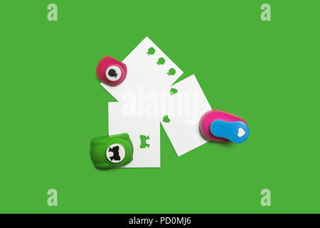Tre piccoli in plastica colorata foro i punciatori con fogli di carta in piedi sullo sfondo verde. concetto di ufficio Cancelleria. spazio libero per il testo Foto Stock
