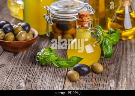 Decapato verde e olive nere in ciotola di legno e olio di oliva in bottiglie rustico Foto Stock