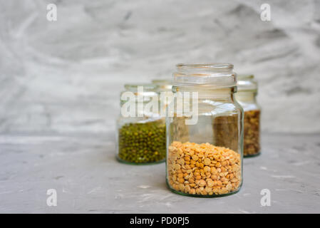 Varietà di cereali in chicchi - mung, secco piselli, lenticchie e ceci in vasi sul cemento grigio sfondo Foto Stock