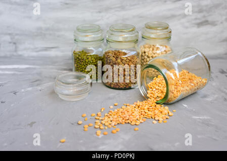 Varietà di cereali in chicchi - mung, secco piselli, lenticchie e ceci in vasi sul cemento grigio sfondo Foto Stock
