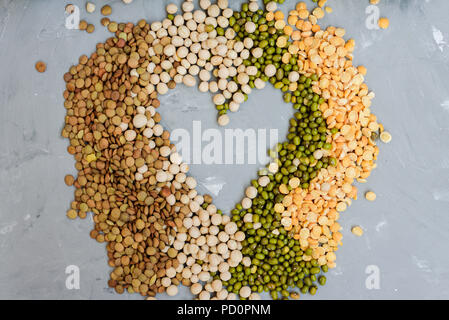 Varietà di cereali in chicchi - mung, secco piselli, lenticchie e ceci in vasi sul cemento grigio sfondo Foto Stock