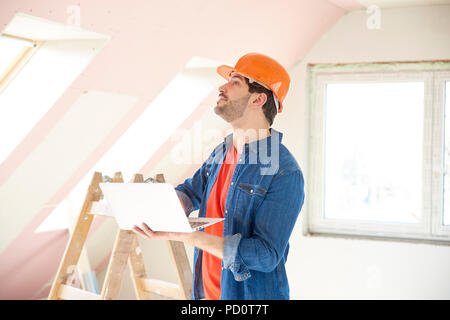 Colpo di giovane ingegnere portatile tenuta in mano mentre si sta in piedi in cantiere e di lavoro. Foto Stock