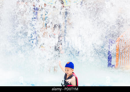 PHUKET, Tailandia - 8 luglio 2017 - Giovane ragazzo asiatico di scappare da spruzzi d'acqua verso il basso dal gioco d'acqua massa alla giungla Splash Water Park a Phuk Foto Stock