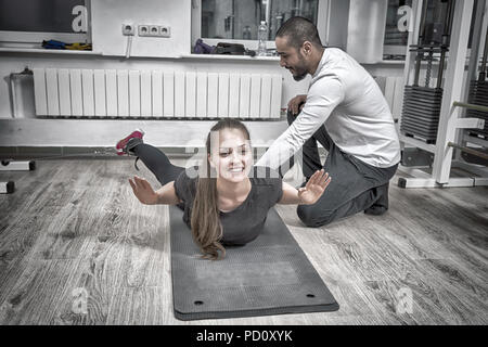 Istruttore assiste la donna esercita sul cavo macchina alla palestra Foto Stock