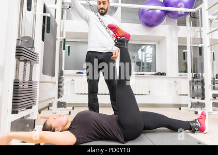 Donna che esercitano le gambe sul cavo crossover macchina con trainer assistere alla palestra Foto Stock