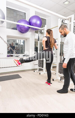 Donna che esercitano le gambe sul cavo macchina mentre personal trainer assiste il suo Foto Stock