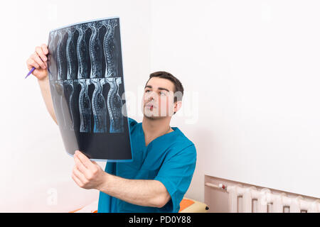 Fisioterapista o medico guardando un ortopedica di raggi x di una colonna vertebrale umana tenendolo come egli lo esamina Foto Stock