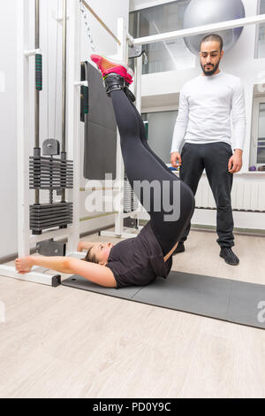 Donna esercitando addominali sul cavo crossover macchina alla palestra con personal trainer Foto Stock