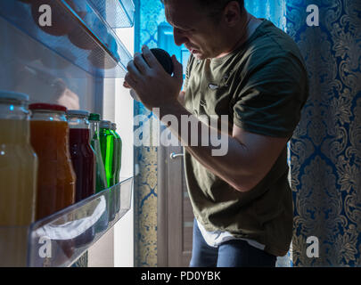 L uomo ricerca dentro il suo frigo durante la notte per qualcosa da mangiare e da bere visto dall'interno del frigorifero in un insolito POV Foto Stock