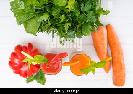 Vista dall'alto in basso di pomodoro e frullati di carota è servita in due bicchieri alti con verdure fresche e un mazzetto di foglia verde erbe assortiti isolati su wh Foto Stock