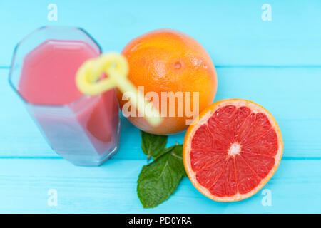 Bicchiere di fresco succo di pompelmo con intero e dimezzato ingredienti pompelmo a fianco sul legno blu visto dal di sopra con la messa a fuoco per la frutta in una hea Foto Stock