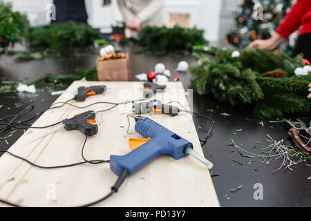 Diverse pistole per colla in primo piano sulla scheda. Produttore della ghirlanda di Natale da rami di pino per le vacanze. Master class sulla realizzazione di ornamenti decorativi. Foto Stock