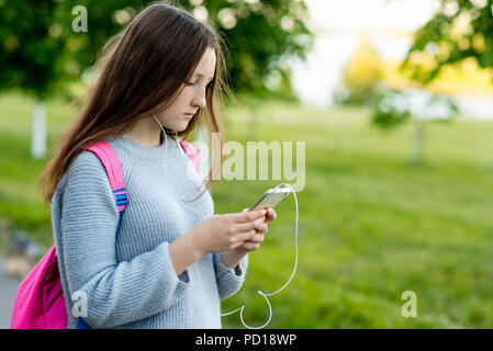 Ragazza schoolgirl studente. In estate sulla strada. Nelle sue mani detiene uno smartphone. Riprodurre musica legge e scrive i messaggi sulle reti sociali. Spazio libero per il testo. Foto Stock