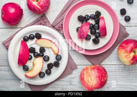 Le mele rosse, more e mirtilli in piastre su un bianco tavolo in legno Foto Stock