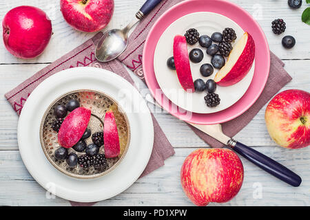 Le mele rosse, more e mirtilli in piastre su un bianco tavolo in legno Foto Stock