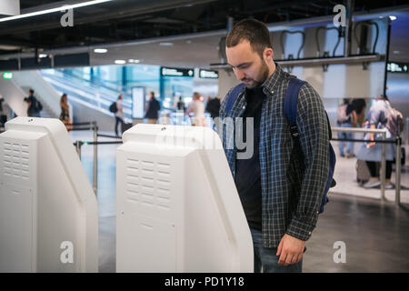 Uomo felice utilizzo della macchina del check-in in aeroporto Come ottenere la carta d'imbarco Foto Stock