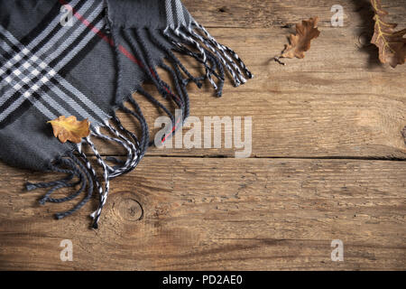 L'autunno. Brown plaid a scacchi a secco con foglie di quercia su sfondo di legno. Foto Stock