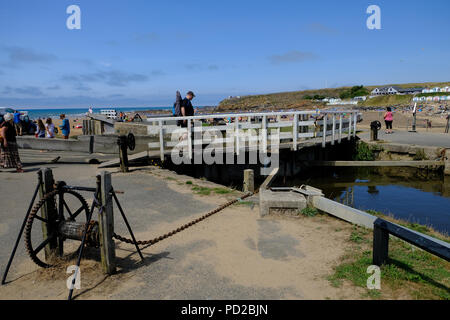 Bude, Cornwall, Regno Unito. Vacanzieri godere il caldo a piedi lungo il canale in Bude e attraversando il bloccaggio del mare Foto Stock