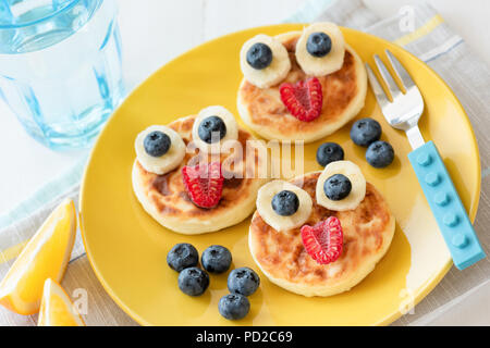 Cibo di divertimento per i bambini. Frittelle con divertenti facce di animali sulla colorata giallo piastra. Per i pasti dei bambini. Messa a fuoco selettiva Foto Stock