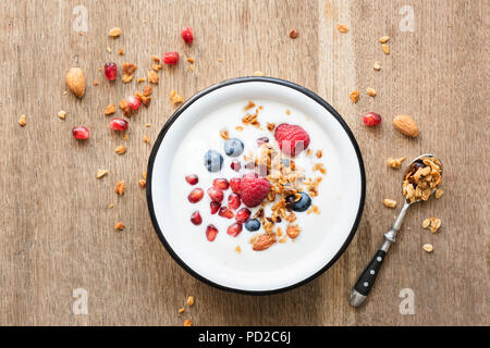 Lo yogurt greco con miele granola, i semi di melograno, mirtilli e lamponi su un tavolo di legno. Vista superiore Foto Stock