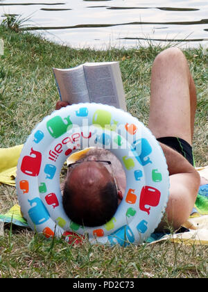 Fotografia dal retro di un uomo con la testa appoggiata in anello di gomma la lettura in vacanza. Close up della lettura in vacanza Foto Stock