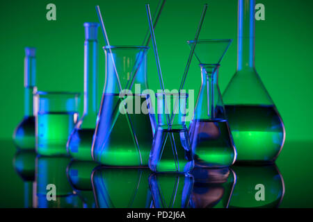 Laboratorio chimico concetto. Esperimento con liquidi. Vetreria di laboratorio. Verde O rosso sfondo. Posto per il logo. Foto Stock