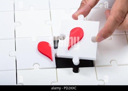 Vista in elevazione di una mano di un uomo il collegamento rotto cuore rosso con puzzle Foto Stock