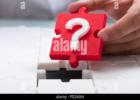 Close-up di mano di una persona immissione punto interrogativo rosso pezzo nel puzzle Foto Stock