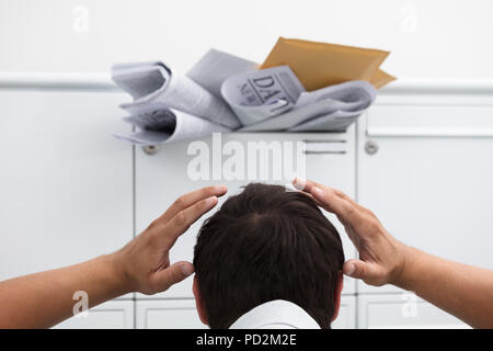 Close-up di uomo con la mano sulla testa nella parte anteriore della cassetta postale di overload con la posta indesiderata Foto Stock