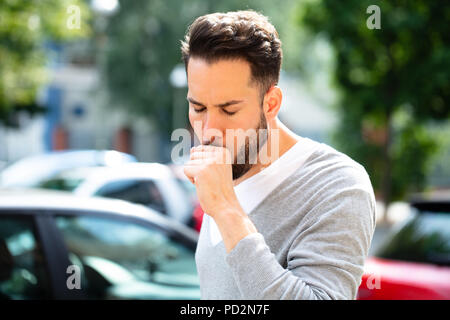 Close-up di un giovane uomo di tosse all'aperto Foto Stock