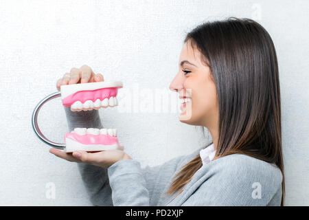 Close up ritratto di attraente ragazza giovane azienda sovradimensionata denti umani protesi.Vista laterale della donna contro la luce sullo sfondo a trama. Foto Stock