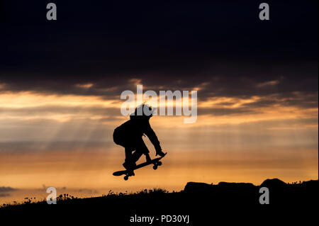 Ragazzo giovane lo skateboard al tramonto, saltando, a metà in aria, Doolin, Clare, Irlanda Foto Stock