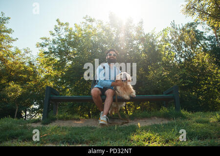 Interessante uomo seduto con il suo cane sulla sedia nel parco en Foto Stock