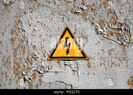 Giallo ad alta tensione di avvertimento triangolo segno su rusty grigio parete in metallo Foto Stock