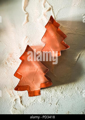 Primo piano di due in rame frese di pasta a forma di albero di Natale, su sfondo bianco con farina intorno, in presenza di luce solare. Foto Stock