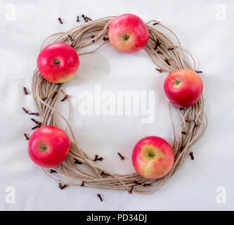 Hessian, spago di corda di iuta corona con le mele rosse e marrone e chiodi di garofano sulle materie di cotone ecru sfondo Foto Stock