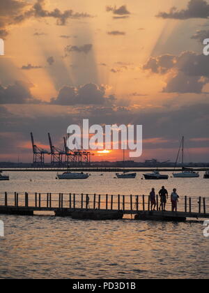 Queenborough, Kent, Regno Unito. Il 6 agosto, 2018. Regno Unito Meteo: il sole al tramonto, Queenborough, Kent. La gru di Thamesport sull'isola di Grain in distanza. Credito: James Bell/Alamy Live News Foto Stock