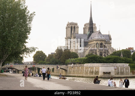 Parigi Notre Dame - la gente camminare lungo la Senna argine sinistro, la cattedrale di Notre Dame in background. Foto Stock