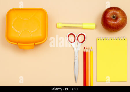 Scatola di pranzo, forbici, colore matite, pennarelli, apple e notebook su sfondo beige. Vista dall'alto. Si torna a scuola concetto. Forniture scolastiche Foto Stock