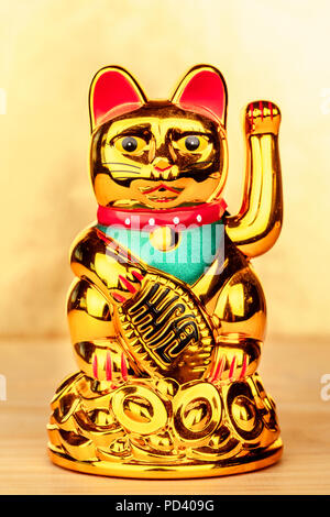 Una foto di Maneki Neko, un Giapponese lucky fatto cenno cat figurina, su uno sfondo dorato con spazio di copia Foto Stock