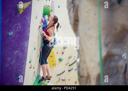 Foto di giovane donna con la fune di sicurezza pratica sulla parete di arrampicata Foto Stock