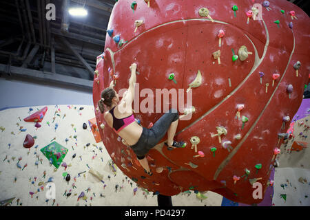 Foto dal retro del giovane atleta ragazza sul rosso sfera di arrampicata in sports hall Foto Stock