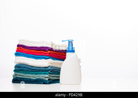 Foto di una bottiglia di sapone liquido colorato e asciugamani puliti su sfondo bianco Foto Stock