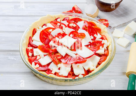 Materie base di impasto per la cottura in una teglia da forno e gli ingredienti per la torta greca con il formaggio e i pomodori, copia spazio, vista dall'alto Foto Stock