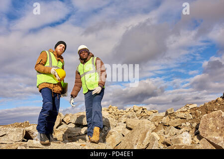 A piena lunghezza ritratto di due operai industriali che indossa giacche catarifrangenti, uno di loro africani, permanente sulla scogliera che si affaccia sulla miniere di minerali su worksit Foto Stock